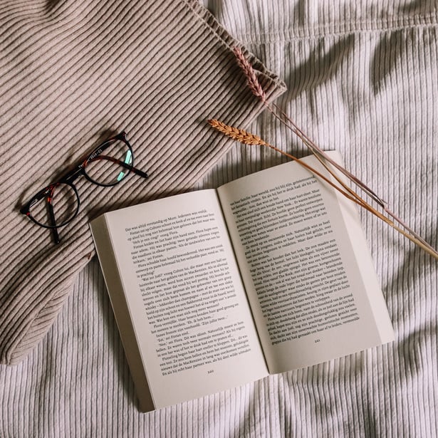 An Open Book Beside Eyeglasses on Brown Fabric